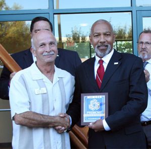 Two men shake hands and display plaque for health center opening