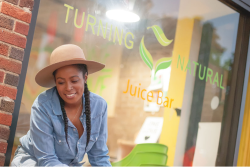 Women wearing hat sitting in front of Turning Natural Juice Bar in Washington, DC, a business which recieved a 2021 Nourish DC grant