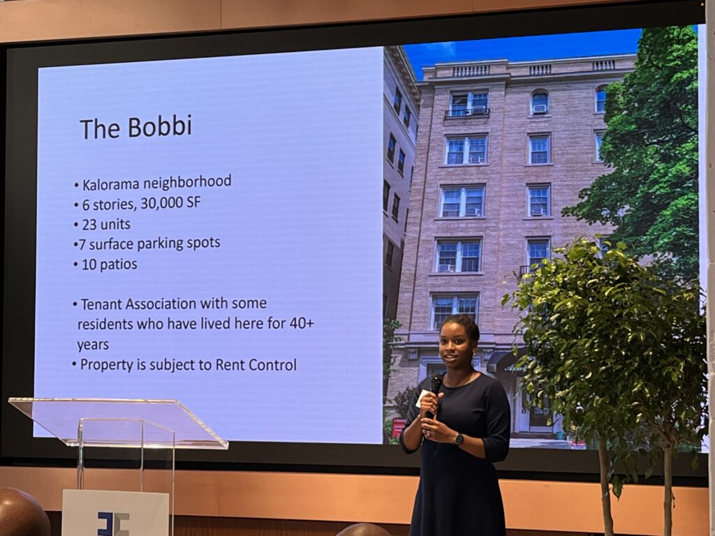 Black woman in a black dress holding a microphone and conducting a presentation