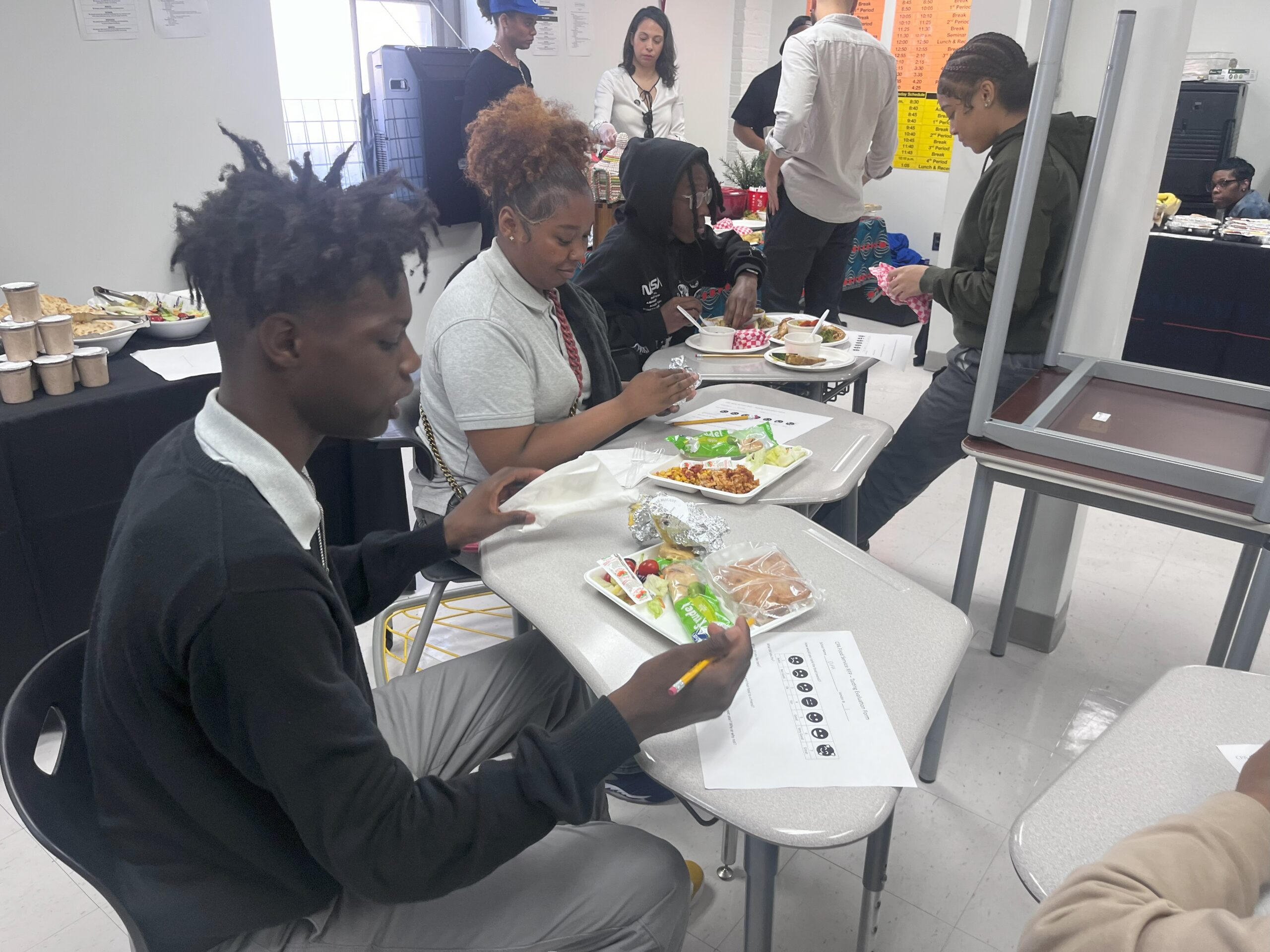 Several people, including students, sit at a table with trays of food. One of the grantees in this year's Co-op Innovation Awards is planning to use their grant to bring down the cost of school meals through group purchasing.