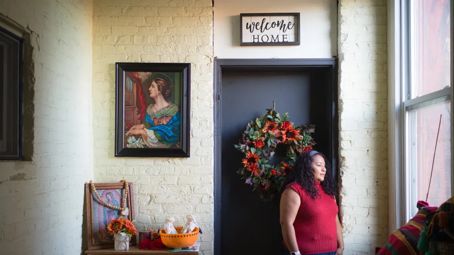 Karen Leon, an owner of Pilsen Housing co-op, wearing red, standing under a sign that reads welcome home